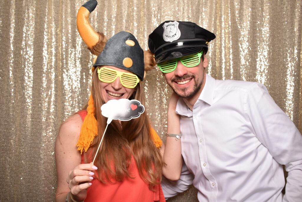 Paar in der Fotobox mit Wikingerhelm und Polizeimütze vor goldenem Hintergrund