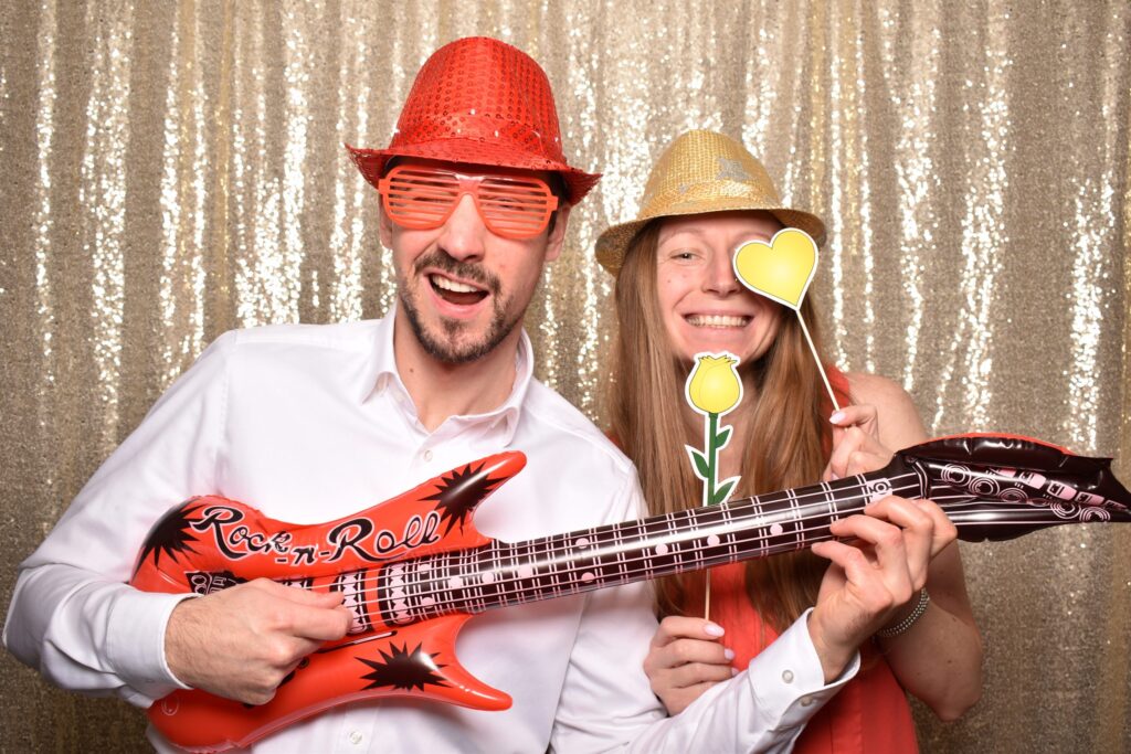 Paar in der Fotobox mit Luftgitarre, Glitzerhut und Herz am Stab