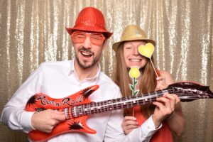 Paar in der Fotobox mit Luftgitarre, Glitzerhut und Herz am Stab