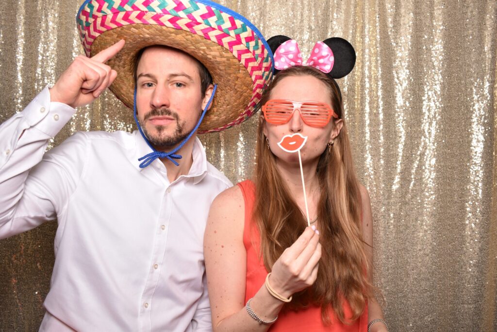 Paar in der Fotobox mit Sombrero und Mausohren vor goldenem Hintergrund