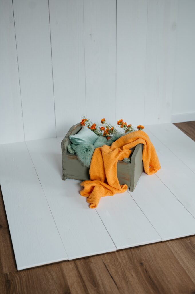 Set im Fotostudio in Denkendorf: kleines Holzbettchen mit orangem Tuch auf hellem Boden