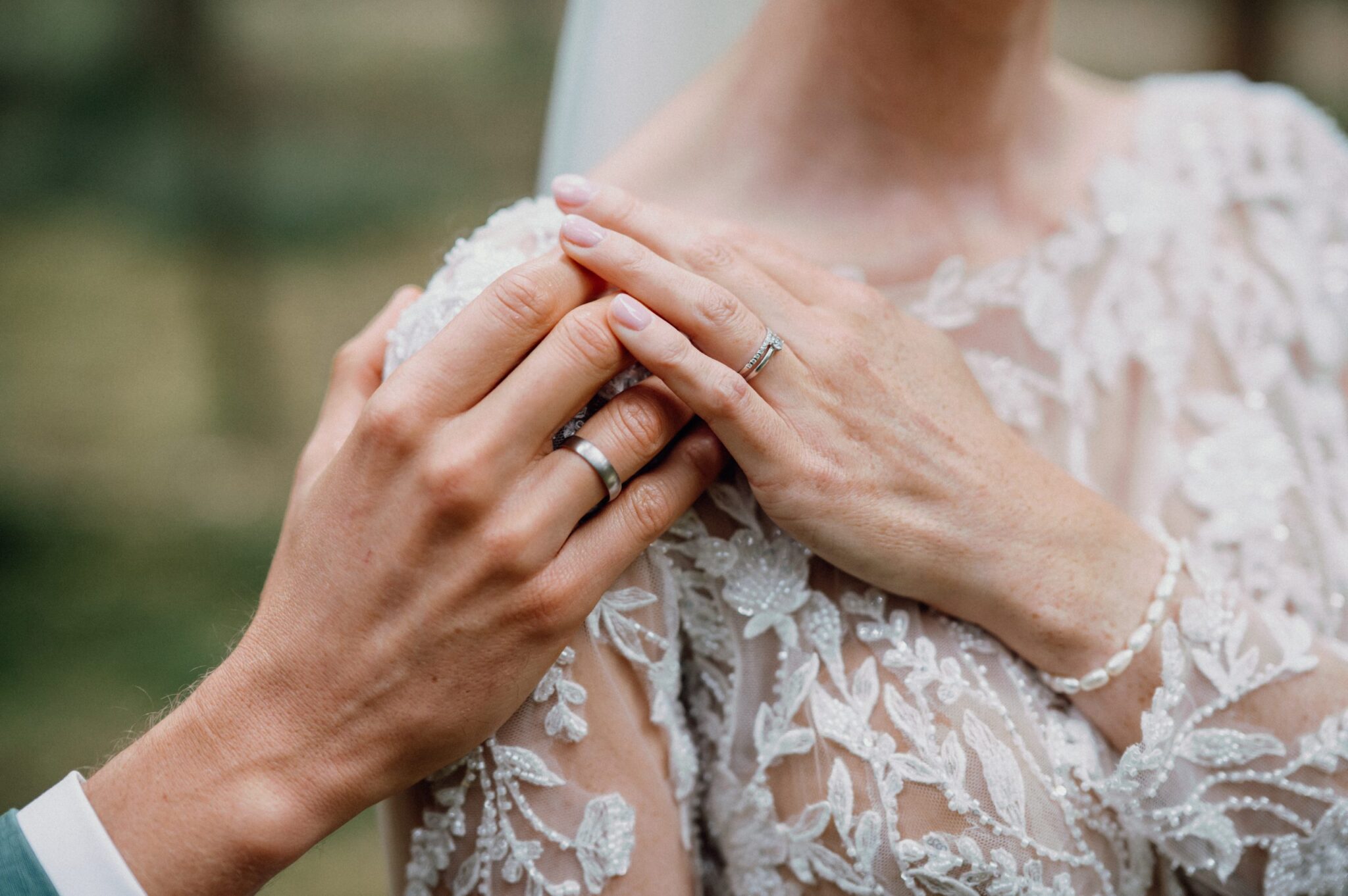 Hände des Brautpaars mit Eheringen auf dem Spitzenkleid der Braut