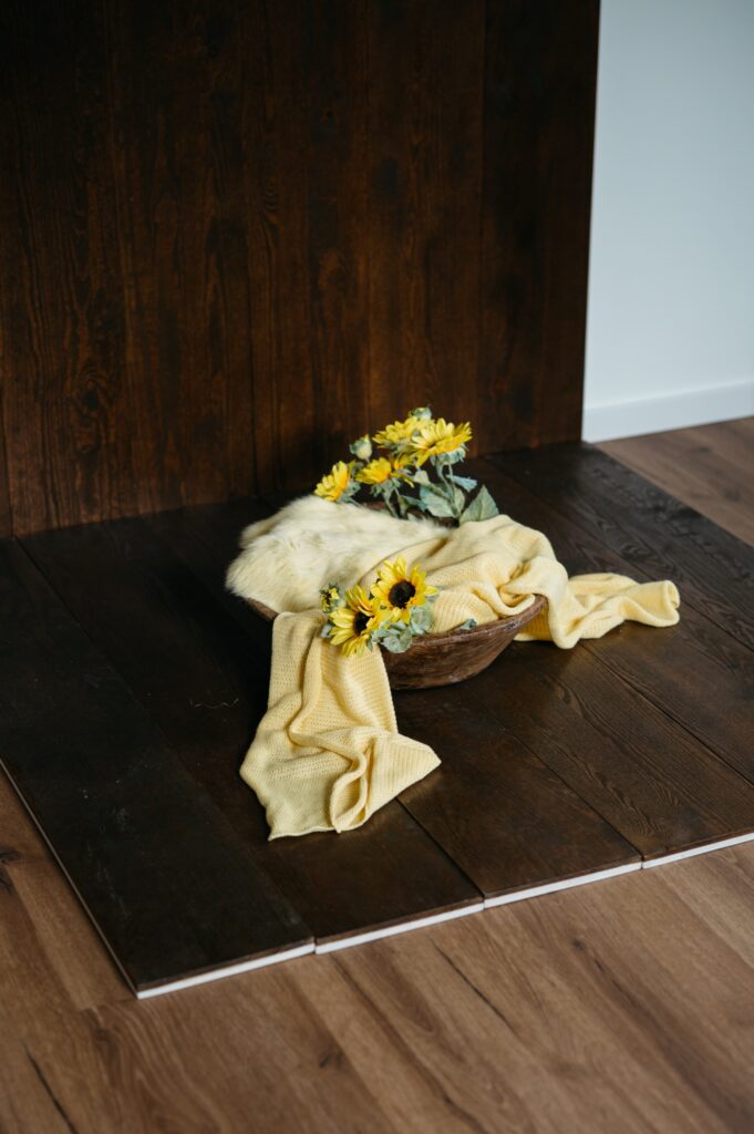 Aufgebautes Set im Fotostudio in Denkendorf: Holzkorb mit hellem Fell, gelbem Tuch und Sonnenblumen auf dunklem Holzboden